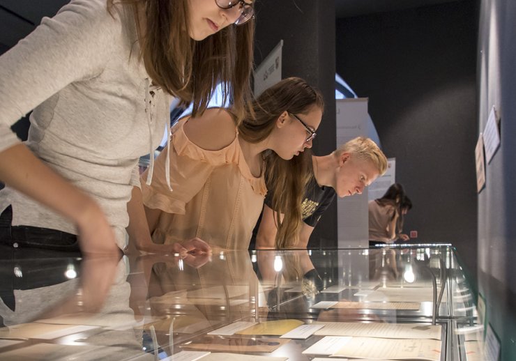 Junge Leute betrachten die Ausstellungsstücke in beleuchteten Schaukästen.