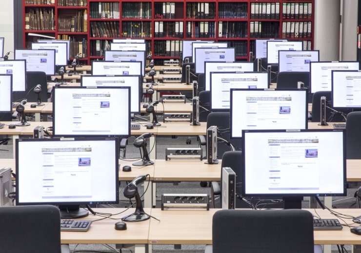 Lesesaal mit mehreren Tischreihen. An jedem Arbeitsplatz befinden sich ein PC, eine Mehrfachsteckdose und ein Barcode-Scanner. 